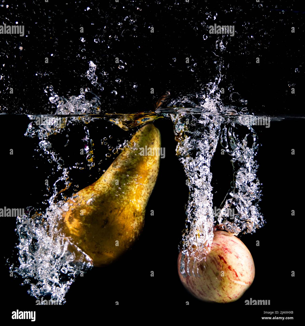 apple e pera si tuffano in acqua, sfondo nero Foto Stock