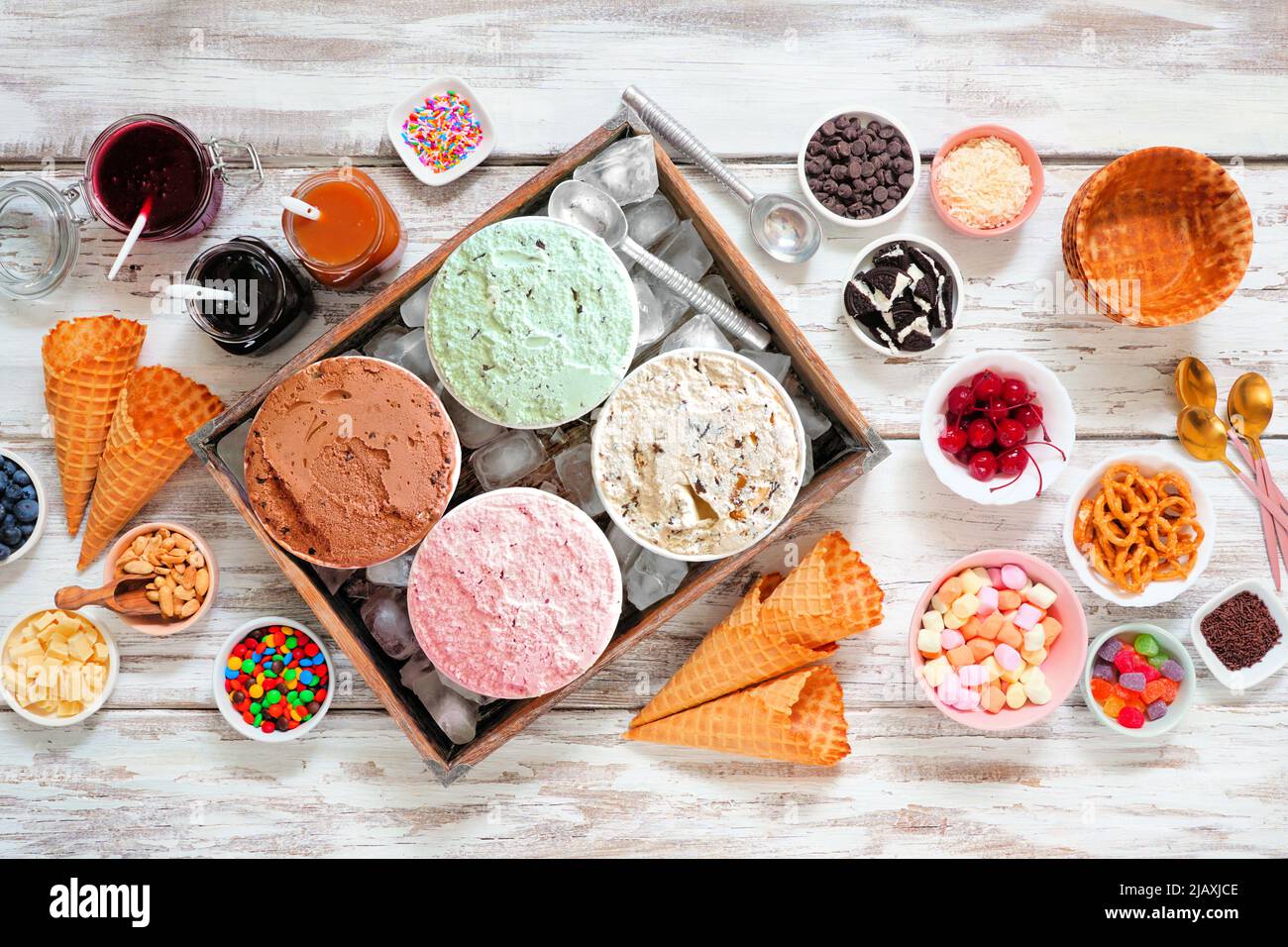 Gelateria estiva con una selezione di sapori di gelato e condimenti da dessert. Vista dall'alto della scena da tavolo su un rustico sfondo di legno bianco. Foto Stock