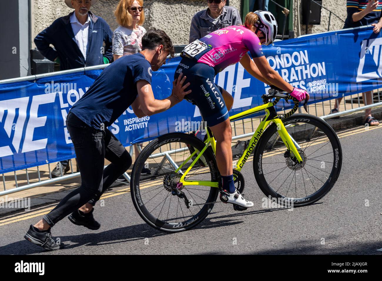 Faller Anastasia Carbonari di Valcar che riceve una spinta dall'equipaggio in bici di ricambio alla gara ciclistica RideLondon Classique stage 1 a Maldon, Essex, Regno Unito Foto Stock