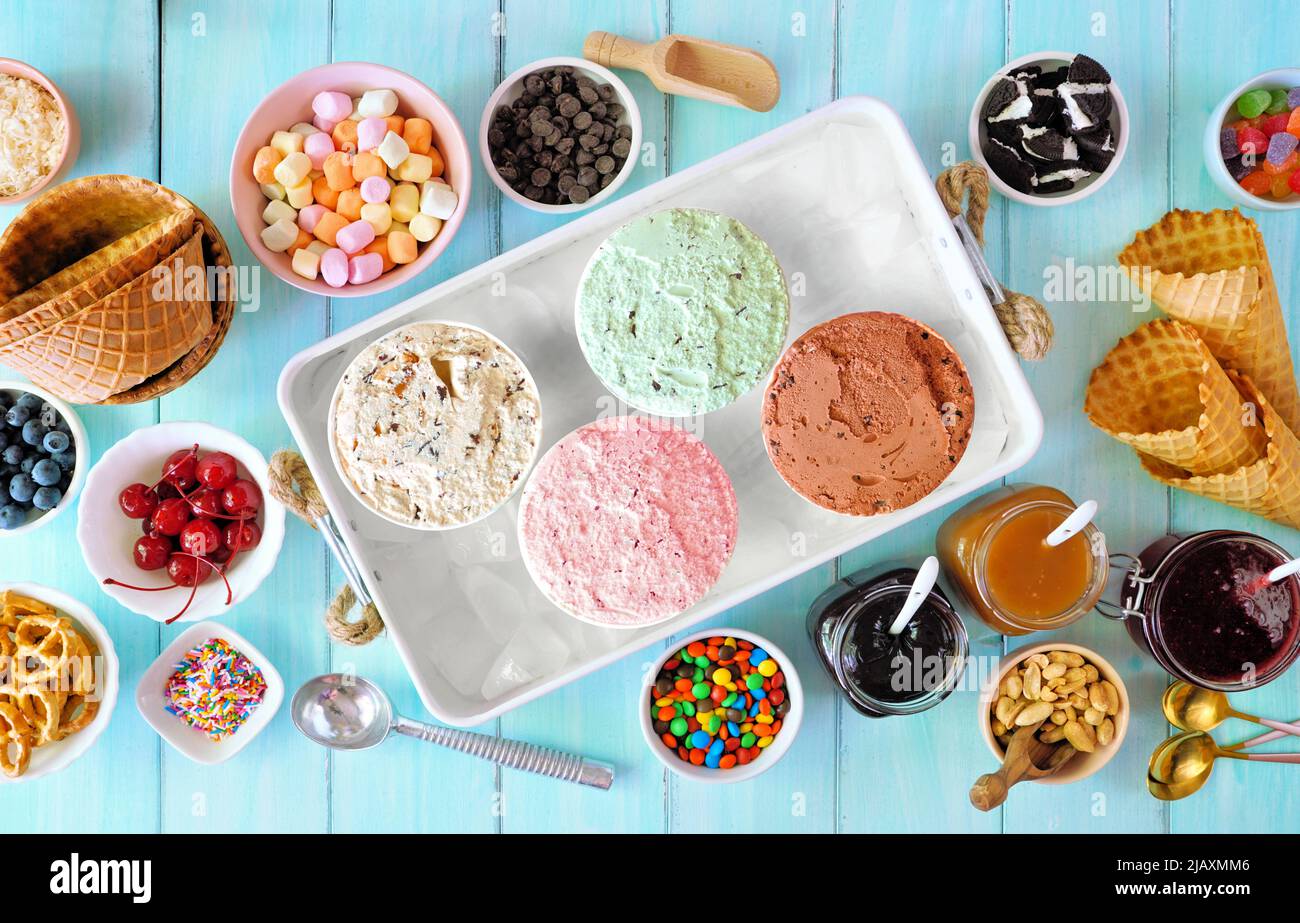 Buffet estivo di gelato con una varietà di sapori e condimenti dolci. Vista dall'alto della scena del tavolo su sfondo di legno blu. Foto Stock