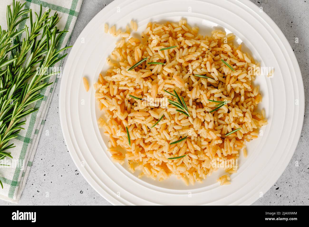 Pilaf di riso con orzo, servito con rosmarino fresco, primo piano su piatto bianco, piatto piatto Foto Stock