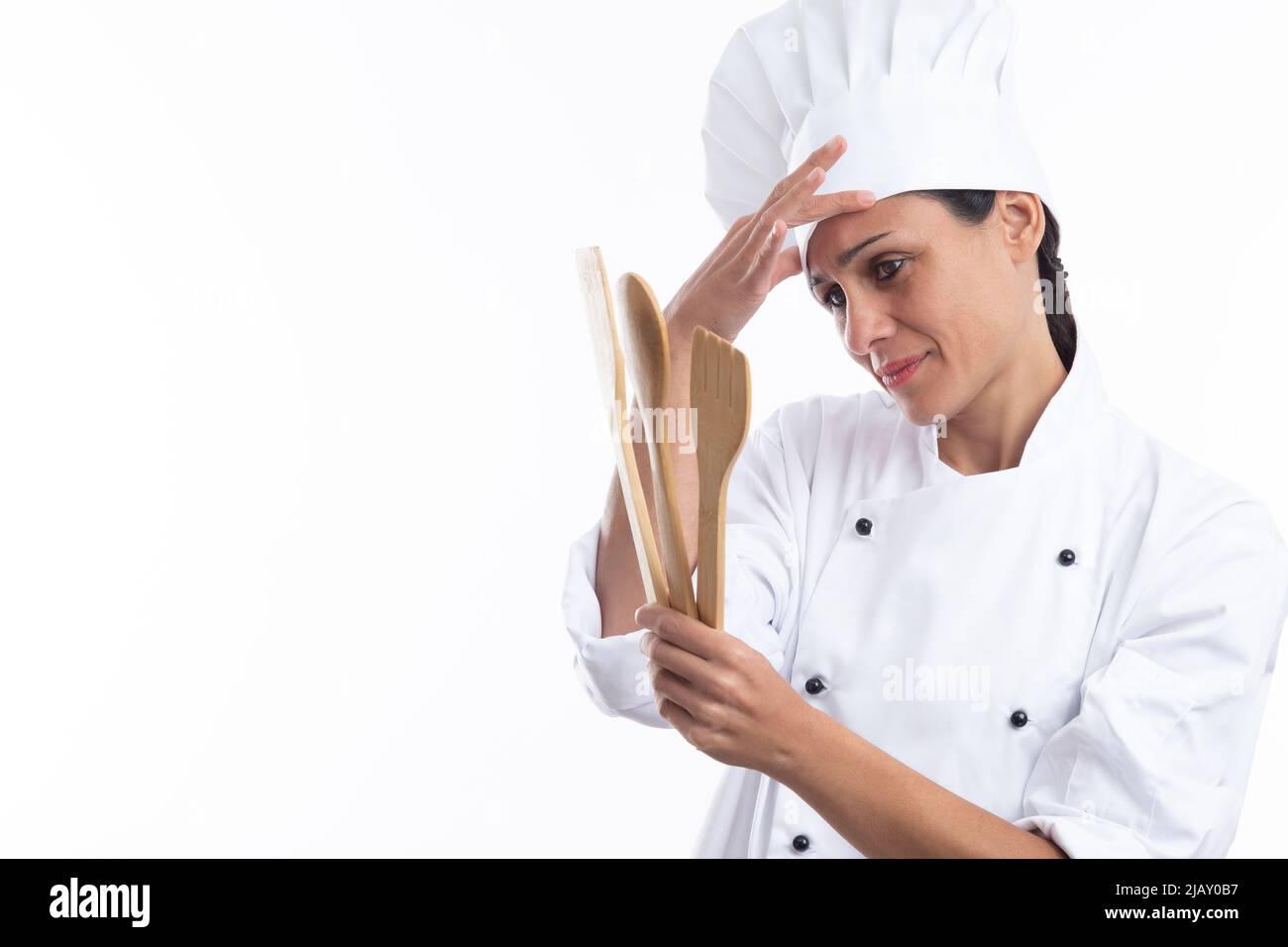 Giovane caucasico giovane chef interessato in vestito chef, tenendo gli utensili da cucina isolati su sfondo bianco con spazio copia. Foto Stock
