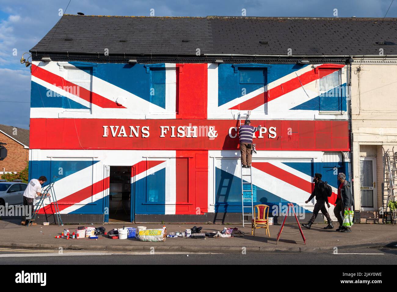 Cradley Heath, West Midlands, Regno Unito. 1st giugno 2022. Warren Rudge, il proprietario del chip shop, mette i tocchi finali sulla Union Jackflag che lui e suo figlio James hanno dipinto sul loro negozio di pesci e chip a Cradley Heath, West Midlands. La bandiera dipinta copre tutta la facciata di Ivan Fish and Chips, comprese le finestre, e ha preso tutto il giorno per completare. 'Ivan's Fish and Chips serve pesce e patatine da 65 anni, ma non tanto quanto sua Maestà. Ma ho sentito dire che la regina è parziale a fish and chips." dice Warren. Credit: Peter Lopeman/Alamy Live News Foto Stock