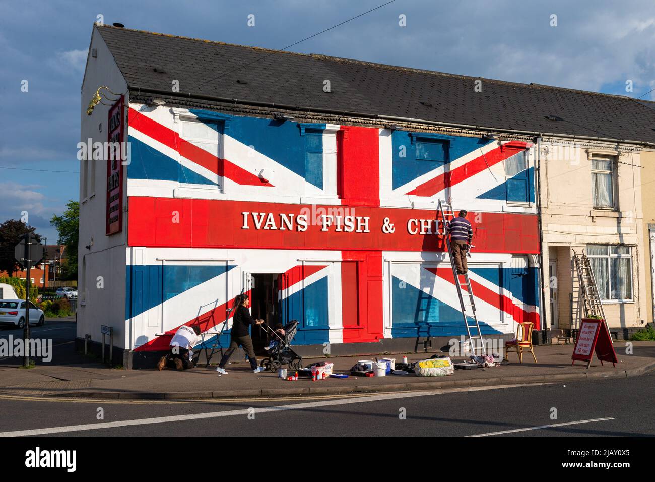 Cradley Heath, West Midlands, Regno Unito. 1st giugno 2022. Warren Rudge, il proprietario del chip shop, mette i tocchi finali sulla Union Jackflag che lui e suo figlio James hanno dipinto sul loro negozio di pesci e chip a Cradley Heath, West Midlands. La bandiera dipinta copre tutta la facciata di Ivan Fish and Chips, comprese le finestre, e ha preso tutto il giorno per completare. 'Ivan's Fish and Chips serve pesce e patatine da 65 anni, ma non tanto quanto sua Maestà. Ma ho sentito dire che la regina è parziale a fish and chips." dice Warren. Credit: Peter Lopeman/Alamy Live News Foto Stock