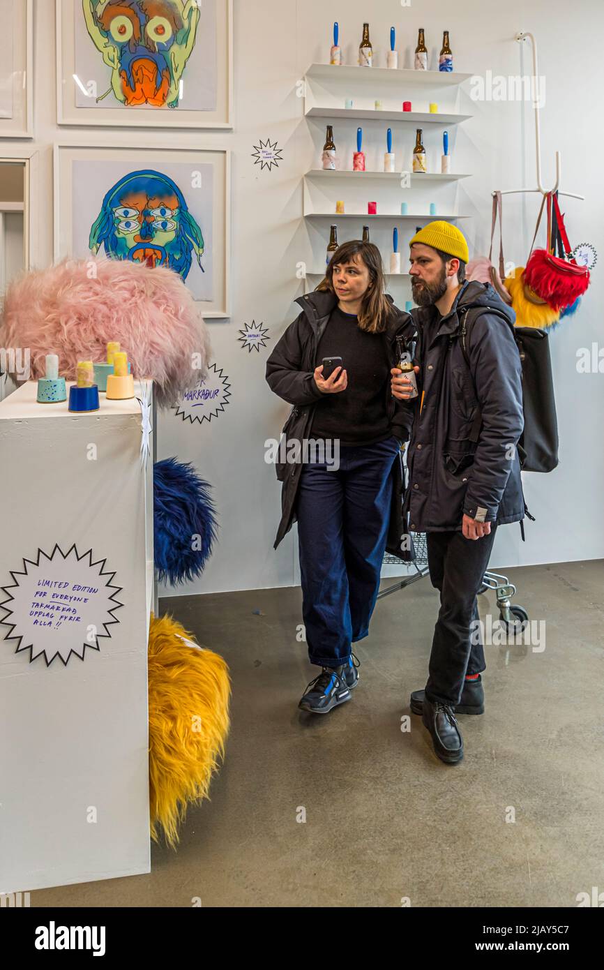 Un uomo con un cappello giallo e uno zaino è in piedi con una compagna davanti allo scaffale a muro che espone bottiglie di birra e oggetti dipinti a colori vivaci nel negozio della Lady Brewery a Reykjavik, Islanda. Un carrello della spesa su ruote è visibile in fondo all'immagine. Foto Stock