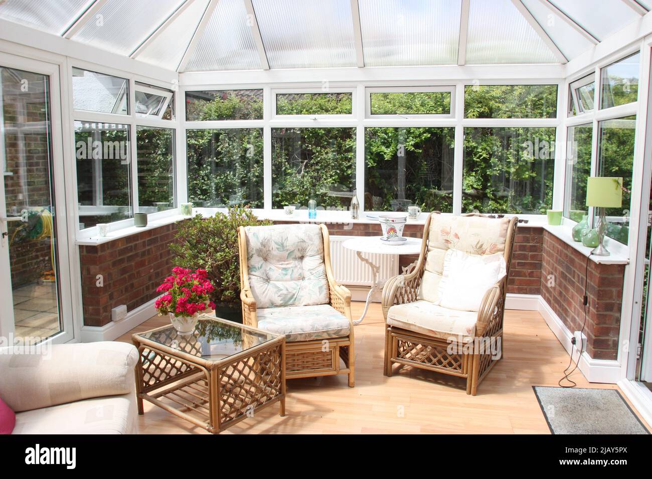 conservatorio con sedie da giardino in vimini, un tavolo di vetro, fiori e finestre Foto Stock
