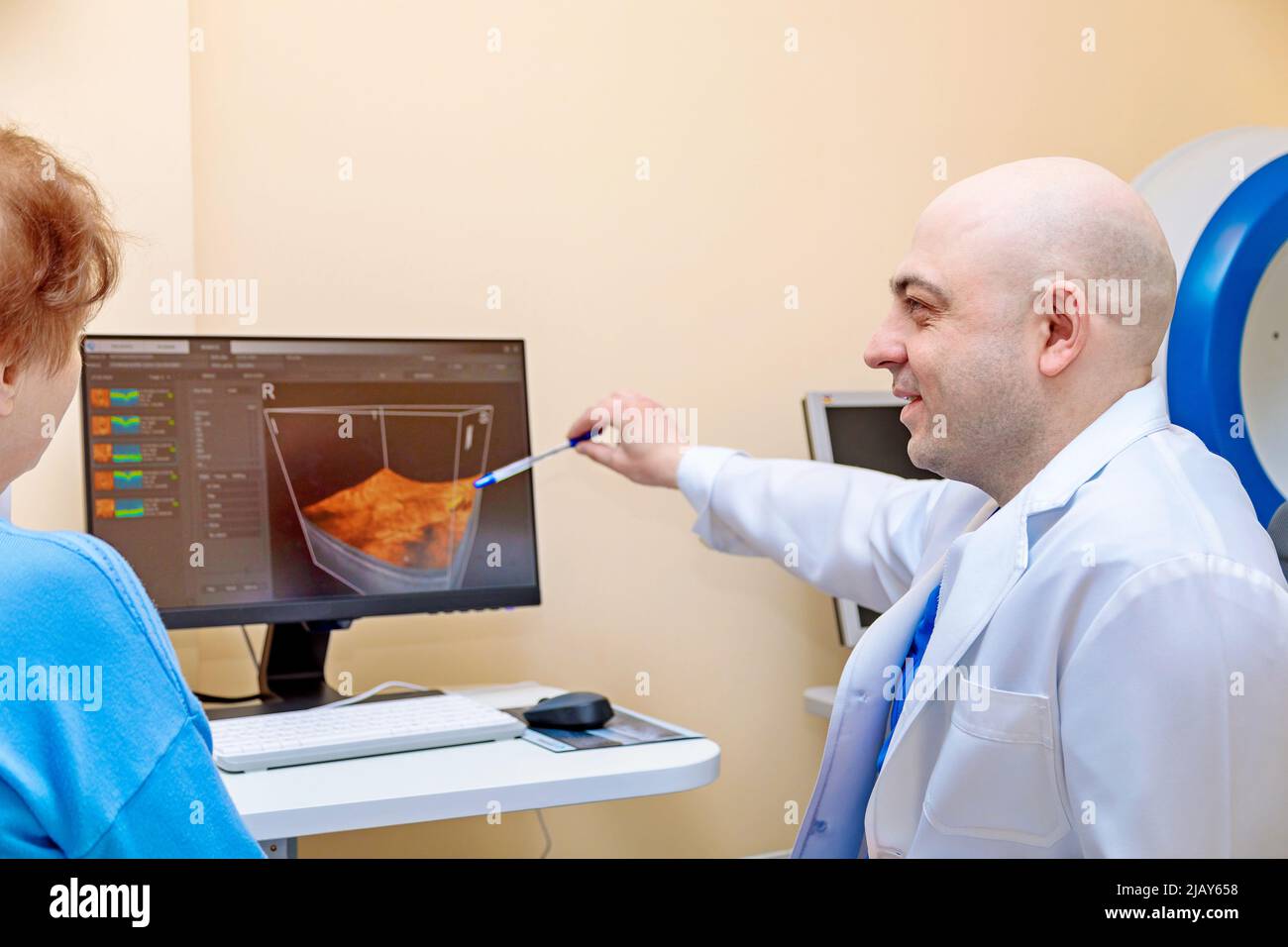 Un oftalmologo maschile spiega i risultati di un esame oculare a una donna adulta, mostrando un disegno su un computer. Foto Stock