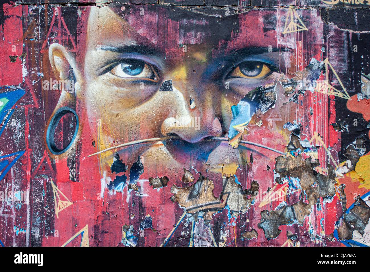 Graffiti molto colorati di un volto etnico con occhi piercing su un muro invecchiato e intemperie Foto Stock