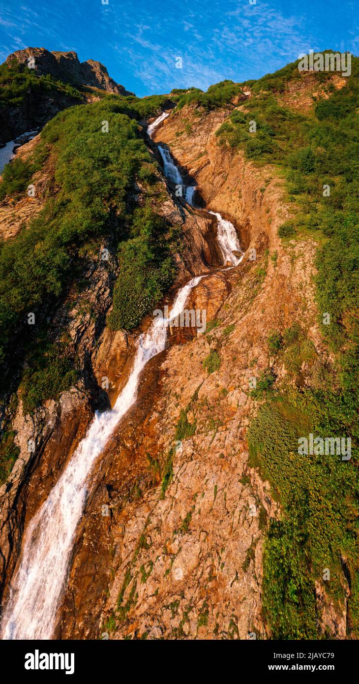 una piccola cascata scorre lungo il pendio di una roccia contro un bel cielo blu Foto Stock