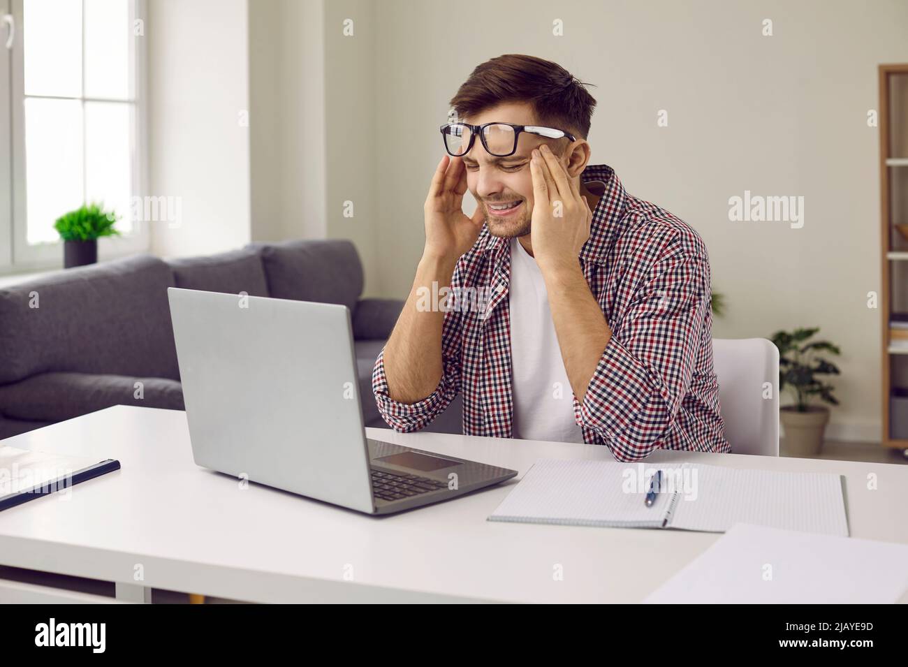Stanco ha stressato l'uomo che lavora su un computer portatile, che soffre di mal di testa e sfrega le sue tempie Foto Stock