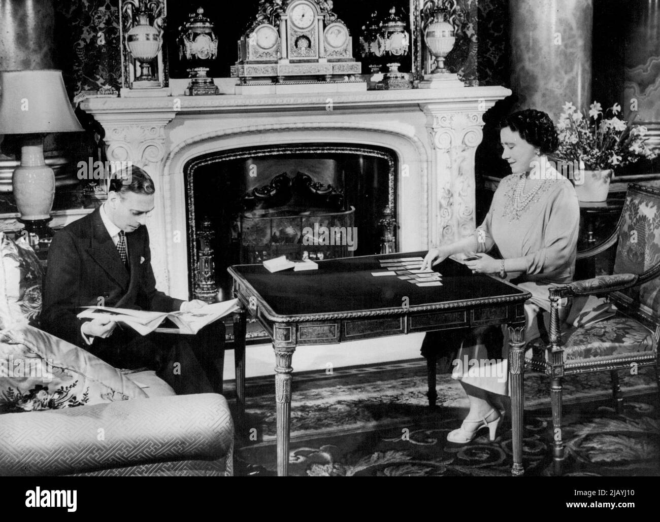 Il Royal Silver Wedding - H.M. la Regina gioca pazienza - un gioco di carte di cui è particolarmente affezionata - mentre il Re legge una rivista. Lunedì prossimo, 26th aprile, le loro maestà Re Giorgio VI e Regina Elisabetta celebrano il loro anniversario di matrimonio del 25th: Il loro matrimonio d'argento. Queste intime fotografie mostrano la coppia reale a casa nei loro appartamenti privati a Buckingham Palace, Londra, e sono state scattate appositamente per l'occasione. Aprile 20, 1948. (Foto di Fox Photos). Foto Stock