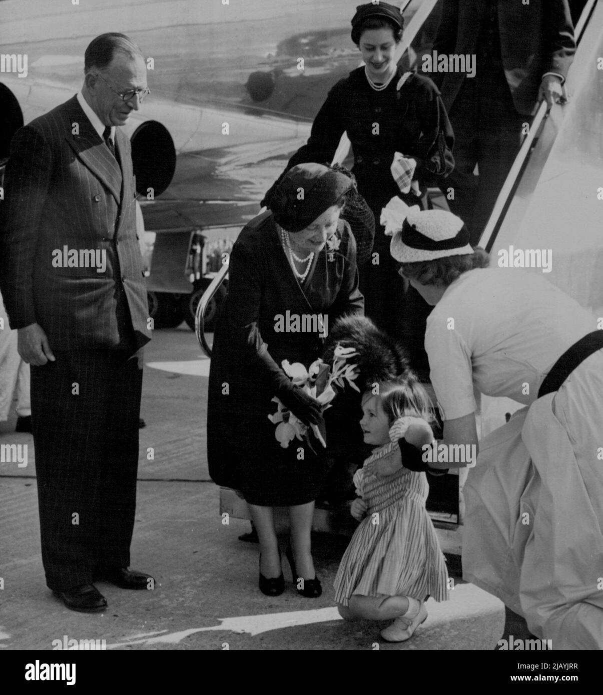 Regina Madre, Principessa Fly in Comet -- la Regina Madre - la Principessa Margaret si vede scendere i gradini dal velivolo accettando un nosegay da Anne De Haviiland, nipote di Sir Geoffrey De Havilland sul suo ritorno a Hatfield dopo il volo. Anne, che ha problemi con la sua curtsey, è assistita da sua madre, la signora Peter De Havilland. Sulla sinistra c'è il signor W.E. Nixon, Amministratore Delegato della De Havilland Company. La Regina Madre e la Principessa Margaret volarono sopra il continetnt in un aereo di linea comet jet di E.O.A.C. al giorno (Venerdì). Maggio 23, 1952. (Foto di Reuterphoto). Foto Stock