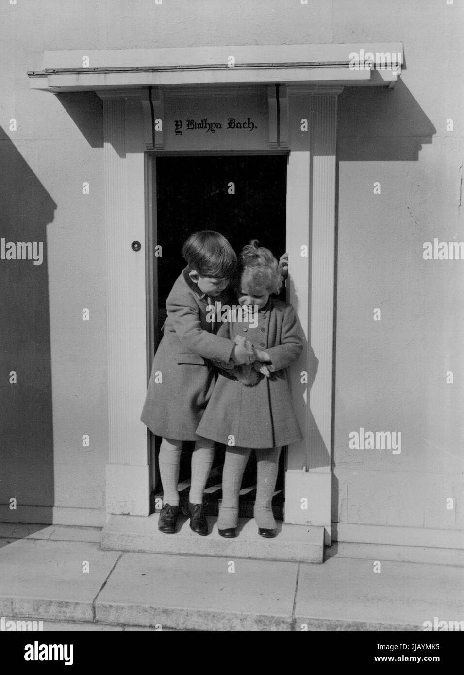 Sui gradini della piccola Casa gallese, il loro cottage in miniatura, il principe Carlo e il principe Anna si ergono insieme, profondamente occupato da un nuovo orsacchiotto. Ottobre 18, 1954. (Foto di Lisa). Foto Stock