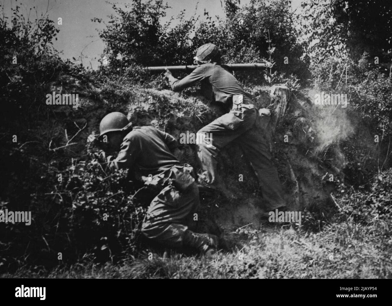Rocket Gun in azione di U. S. -- sviluppato come un'arma anti-serbatoio per i fanti, il lanciarazzi dell'esercito degli Stati Uniti è ora usato efficacemente per distruggere le colonne di calcestruzzo, le pareti di mattone ed i ponti. In questa foto un equipaggio di razzo dietro un hedgerow sta sparando sui tedeschi in Francia. Il fucile pesa poco più di un fucile e lancia proiettili a razzo traforanti. È trasportato da un uomo che lo mira e lo spara sopra la sua spalla mentre l'altro alimenta i razzi nella culatta. Il guscio ha una bassa velocità e può essere guardato in volo ma colpisce con la forza di un guscio di 75 mm. Sviluppato dalla U Foto Stock