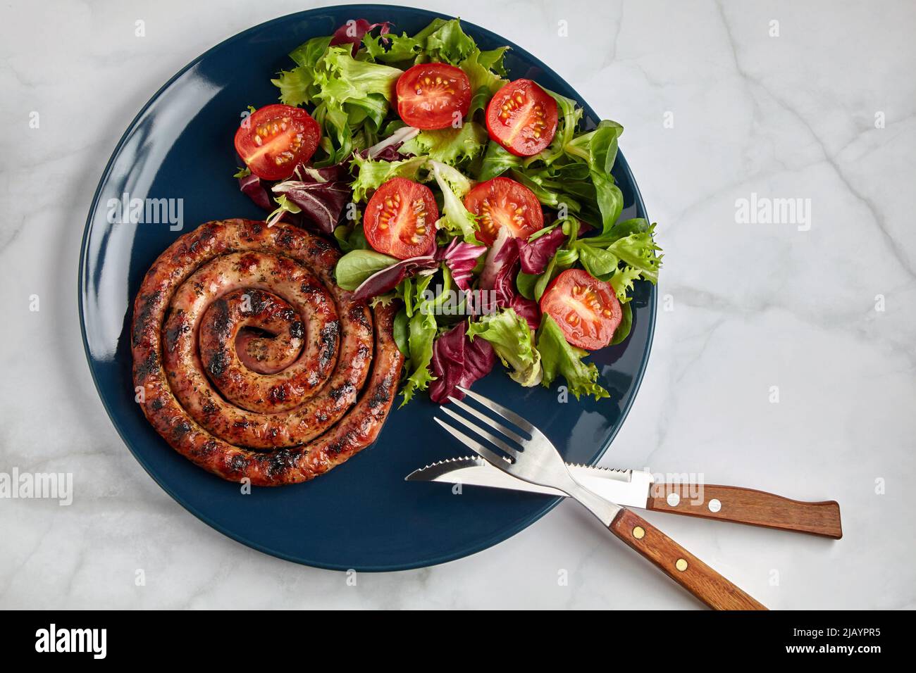 Salsiccia alla griglia con pomodori e erbe tritati su un piatto blu su un tavolo leggero Foto Stock