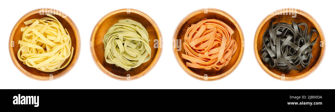 Tagliatelle in quattro colori diversi, intrecciate in nidi, in ciotole di legno. Pasta tradizionale italiana all'uovo cruda e secca. Foto Stock