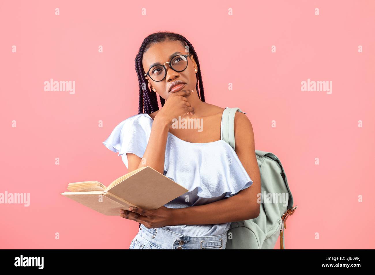 Studentessa femminile nera pensiva con zaino che tiene un libro di testo aperto, pensa all'assegnazione, studia per l'esame Foto Stock