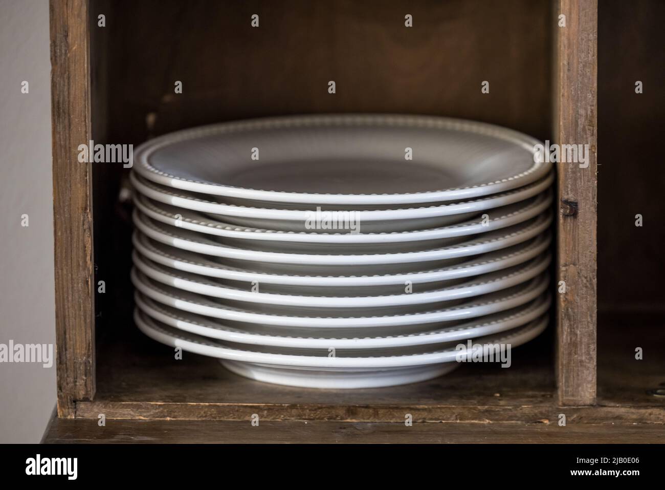 Una pila di piatti da pranzo in porcellana bianca in un armadietto di legno in una casa o in un ristorante Foto Stock
