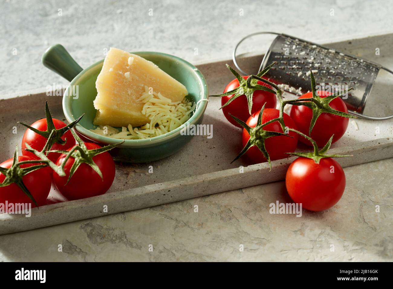 Alto angolo di pomodori freschi messi sul tavolo con formaggio grattugiato in ciotola Foto Stock