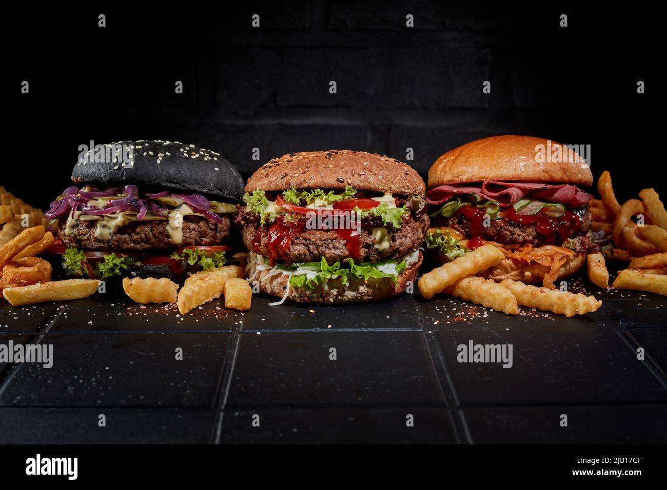 Hamburger assortiti e patatine fritte sul tavolo su sfondo scuro in studio Foto Stock