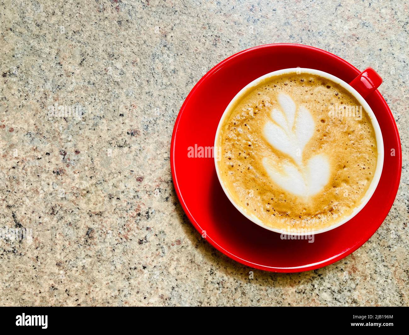 Un caffè bianco piatto in una tazza rossa e un piattino. Arte decorativa del caffè formata nella schiuma del caffè. Foto Stock