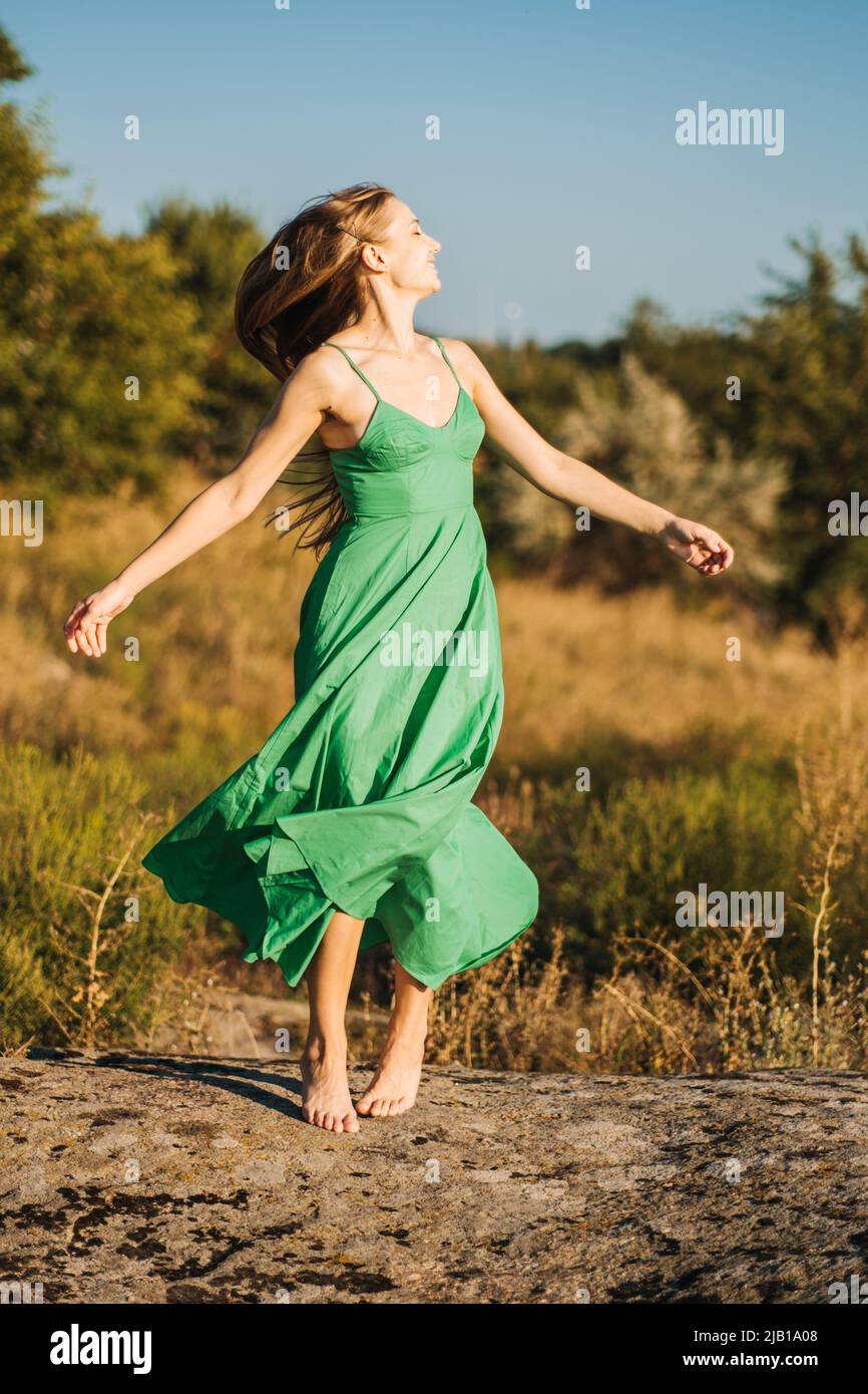 Donna a piedi nudi in abito verde godendo la natura. Terapia della natura, ecoterapia, pratica di essere in natura per stimolare la crescita e la guarigione, salute mentale Foto Stock