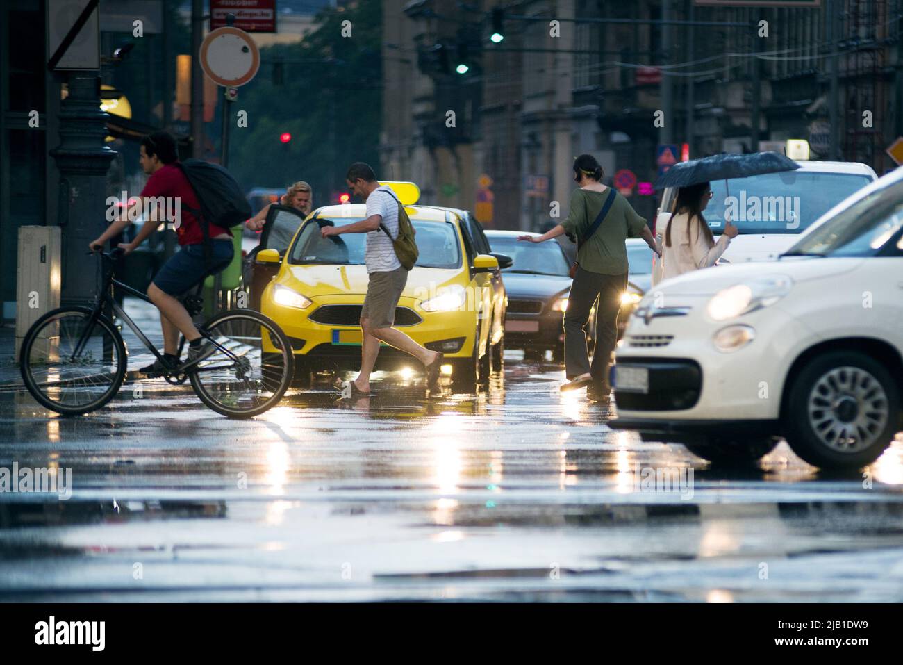 Pioggia in città. Persone che attraversano la strada, saltando sopra le pozzanghere Foto Stock