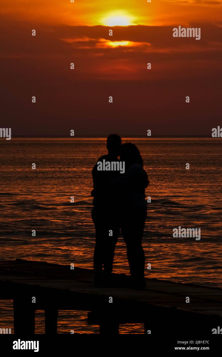 due amanti che si stancano il sole tramontato sul mare Foto Stock