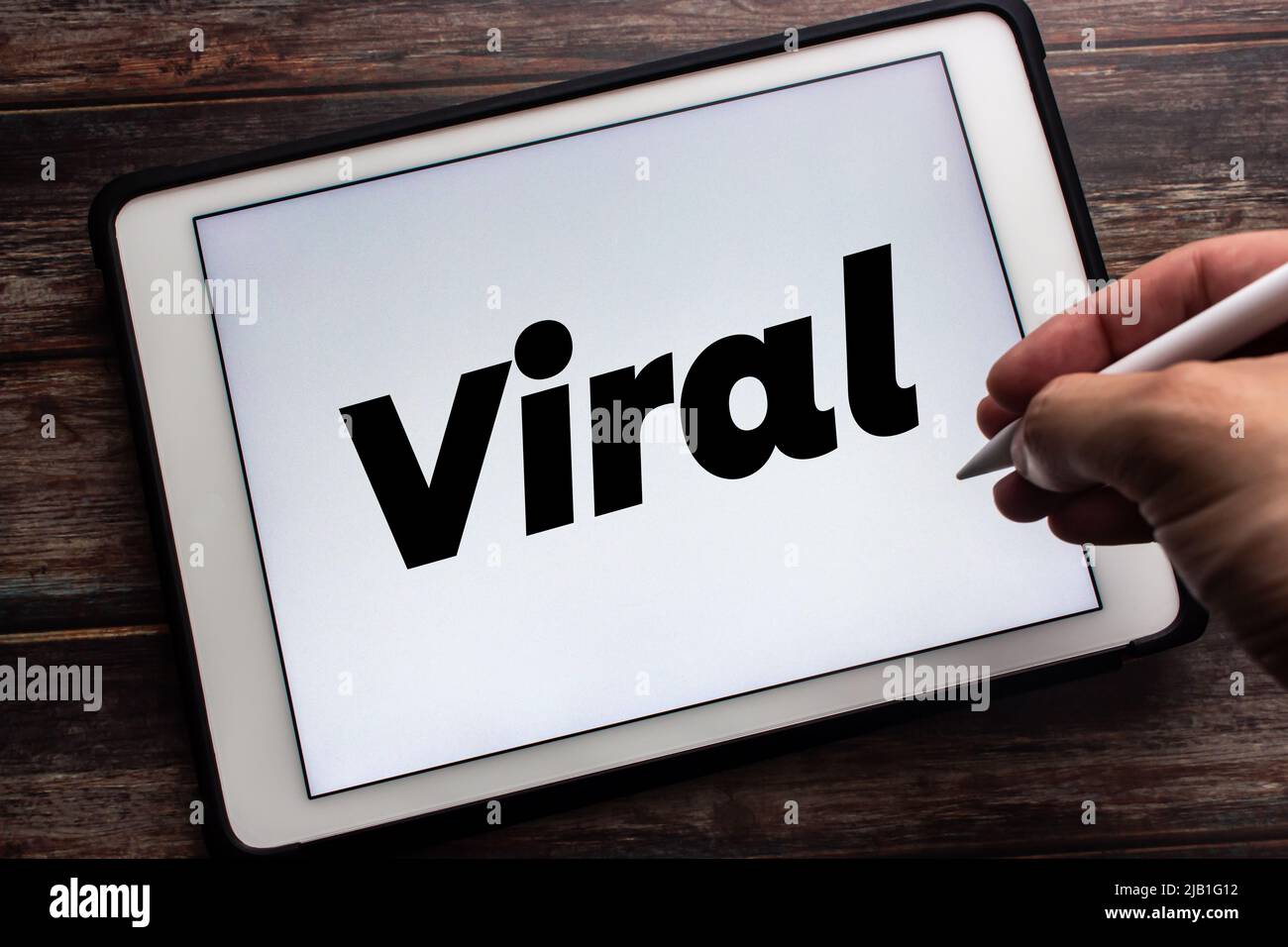 Tablet con la parola chiave "virale". Uomo che tiene la penna stilo wireless nell'immagine. Social media, condivisione e moderno concetto di tendenza tecnologica Foto Stock