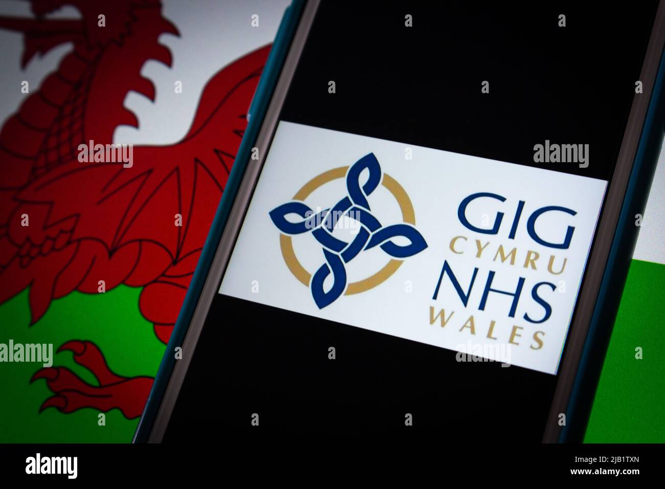 Kumamoto, GIAPPONE - Sep 6 2021 : logo closeup di NHS Wales (gallese: GIG Cymru), il sistema sanitario finanziato pubblicamente in Galles, su iPhone sulla bandiera gallese. Foto Stock