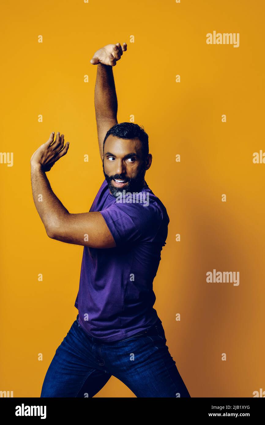 bell'uomo in una t-shirt viola con le braccia sollevate in posa su uno studio di sfondo giallo Foto Stock