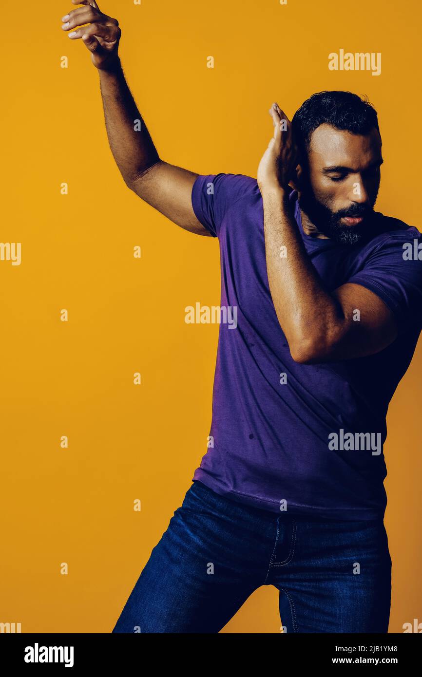 ritratto di un bel giovane adulto sensibile che balla con t-shirt viola su uno studio di sfondo giallo Foto Stock