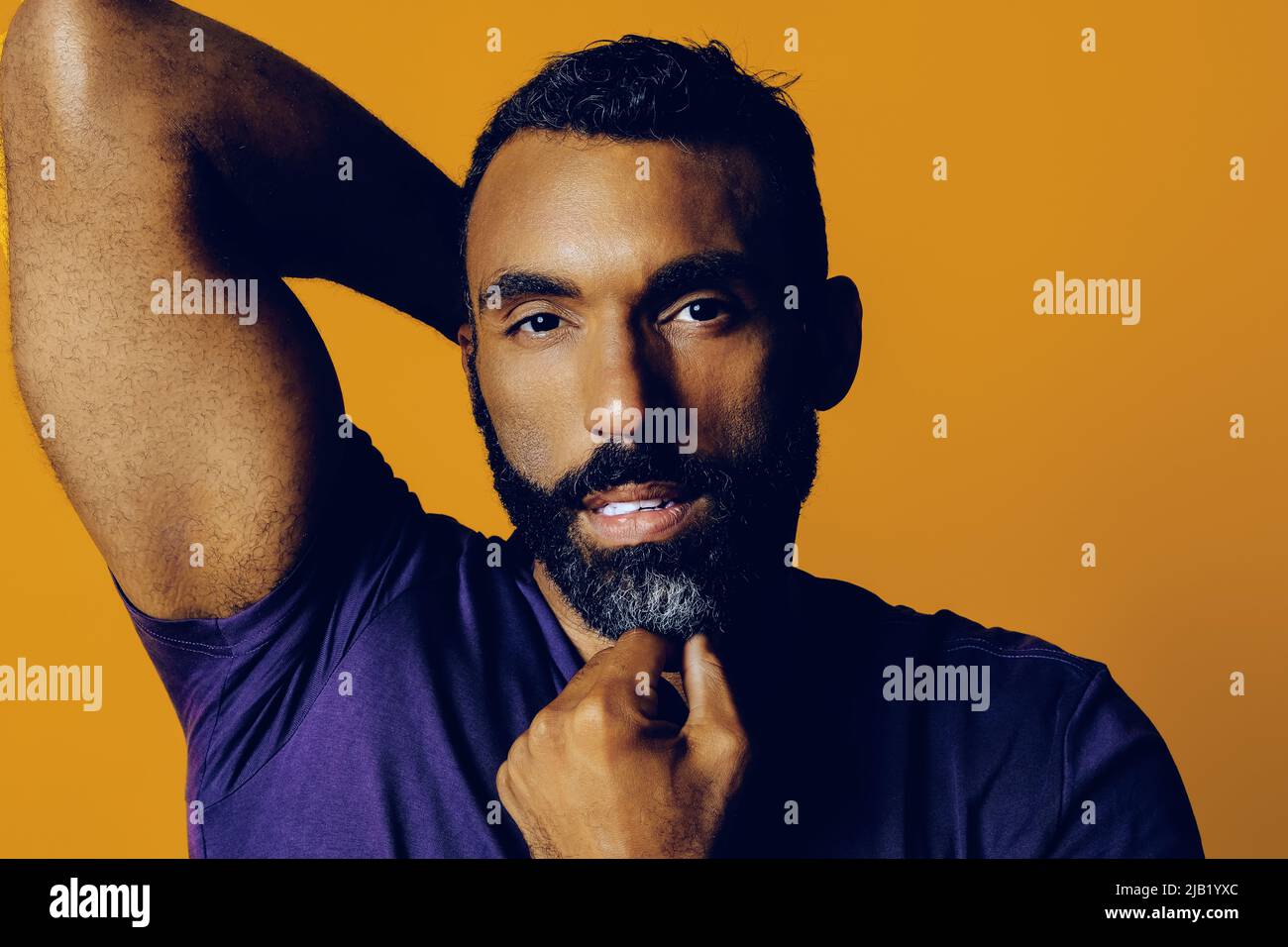 primo piano di un uomo adulto sensibile e premuroso con una barba e una mano baffi sul mento guardando camera studio giallo Foto Stock
