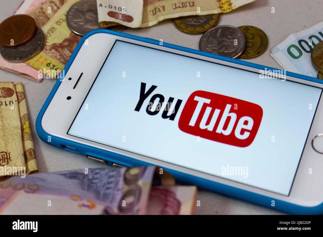 Il logo di YouTube su un iPhone con denaro casuale (banconote e monete). YouTuber, Vtuber e influencer business per il concetto di monetizzazione Foto Stock