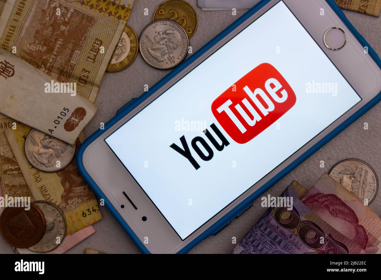 Il logo di YouTube su un iPhone con denaro casuale (banconote e monete). YouTuber, Vtuber e influencer business per il concetto di monetizzazione Foto Stock