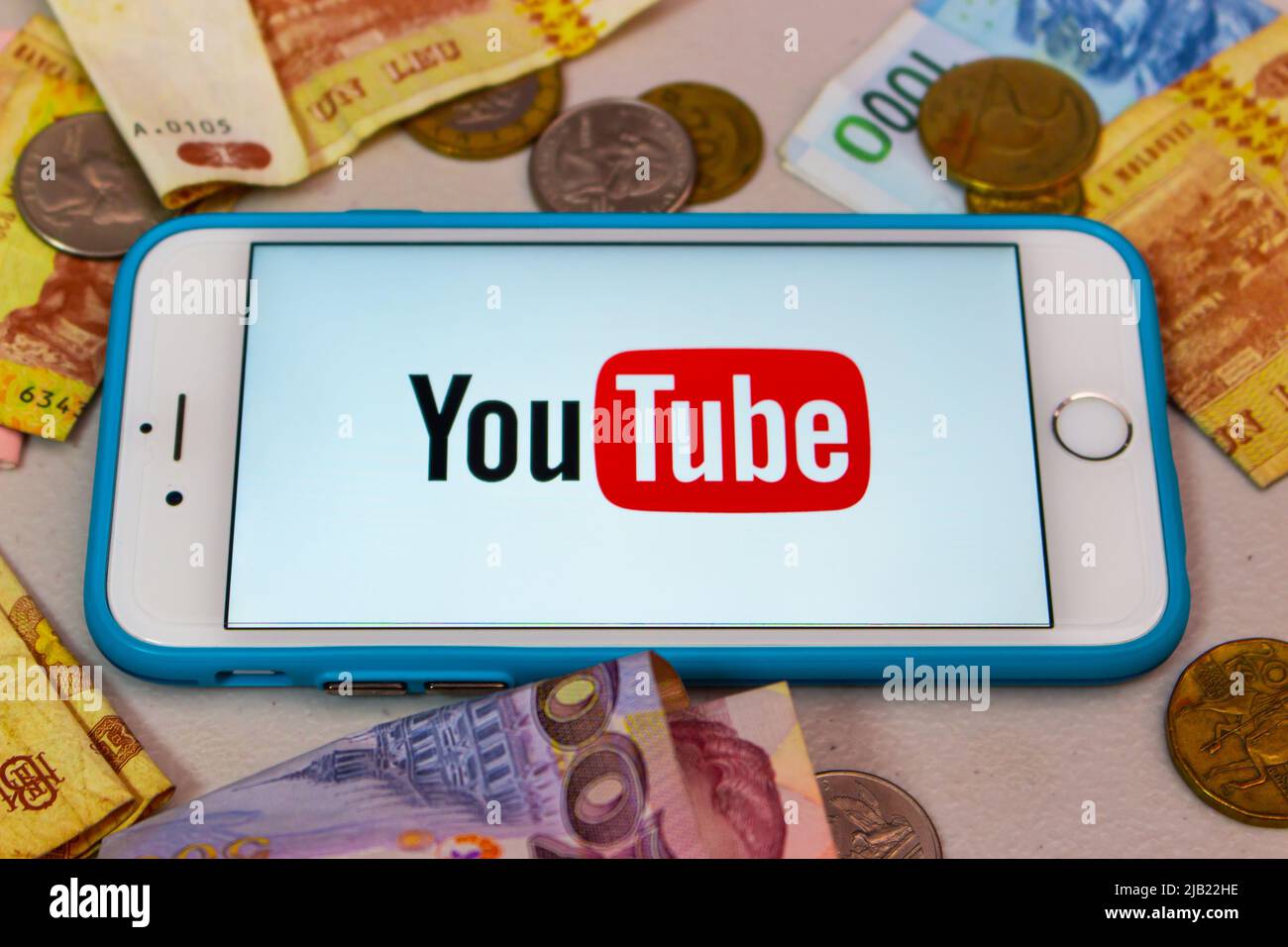 Il logo di YouTube su un iPhone con denaro casuale (banconote e monete). YouTuber, Vtuber e influencer business per il concetto di monetizzazione Foto Stock