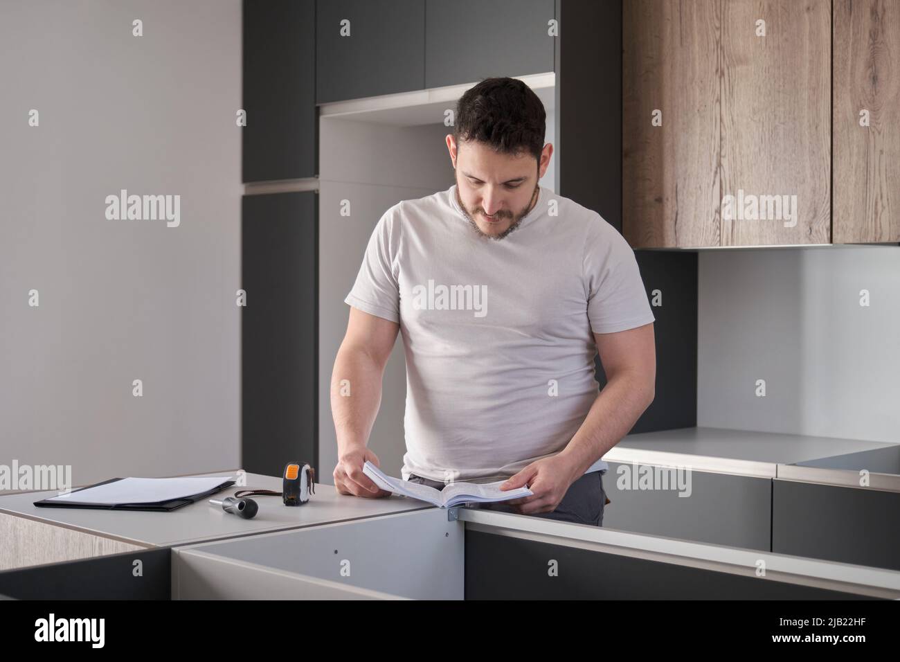 Giovane uomo latino leggere il manuale di istruzioni prima di installare i mobili in cucina. Foto Stock