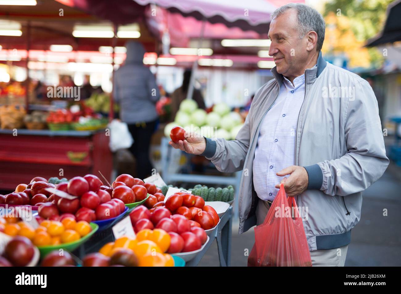 Uomo che sceglie i pomodori in gregrocery Foto Stock