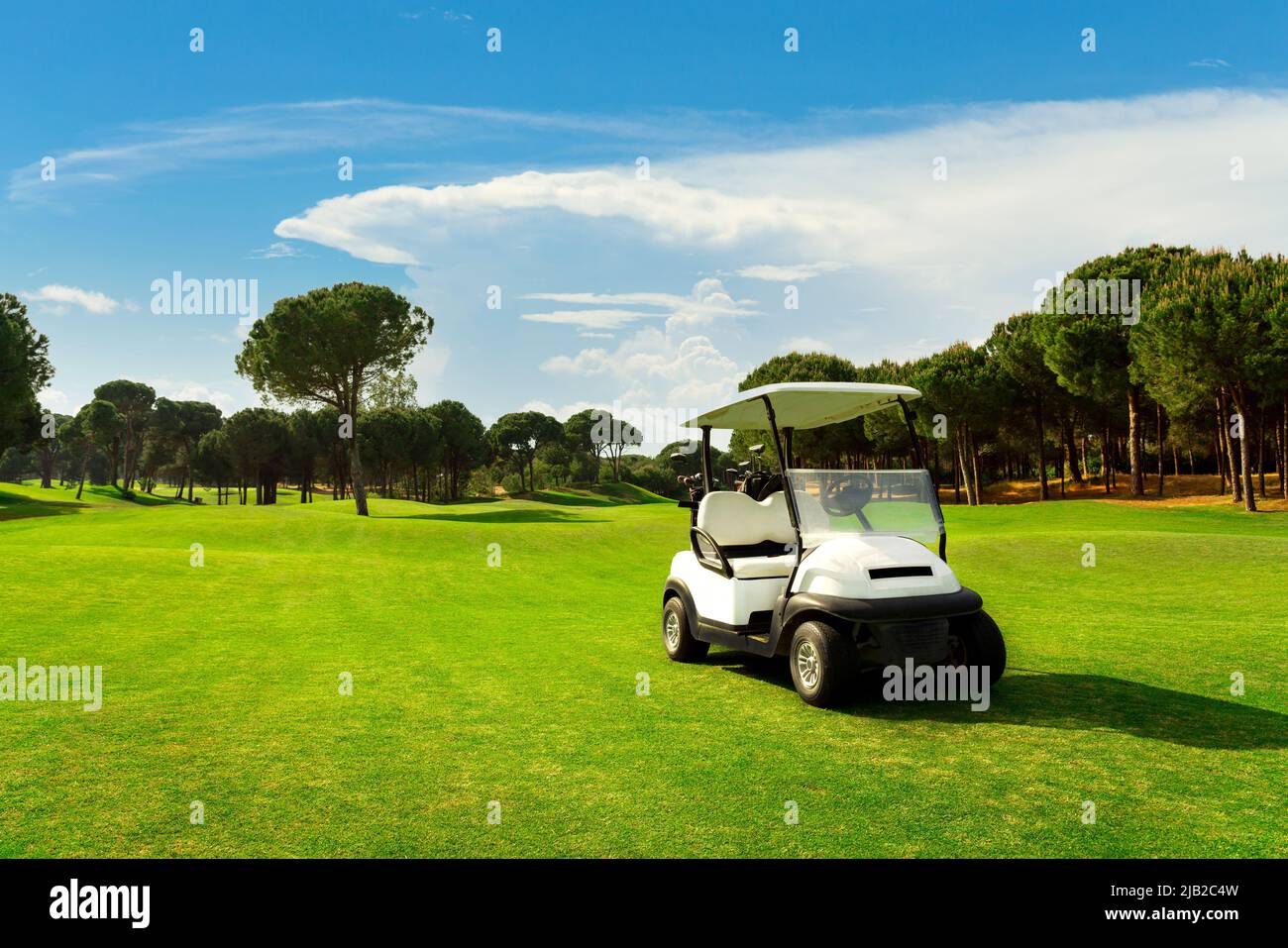 Golf cart nel fairway del campo da golf con erba verde con cielo nuvoloso e alberi al tramonto Foto Stock
