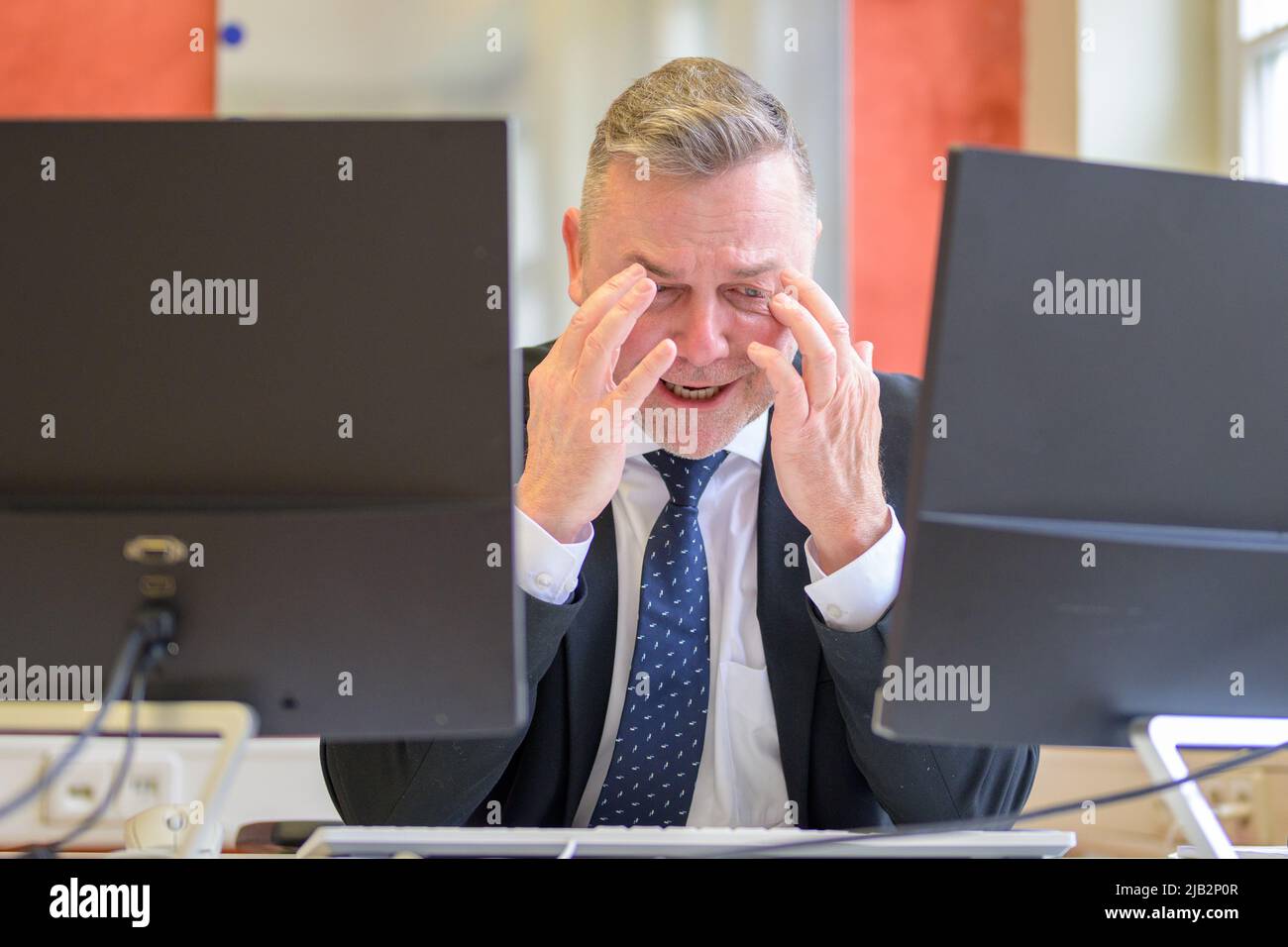 Stressato uomo d'affari stressato strofinando i suoi templi seduti al suo computer in ufficio Foto Stock