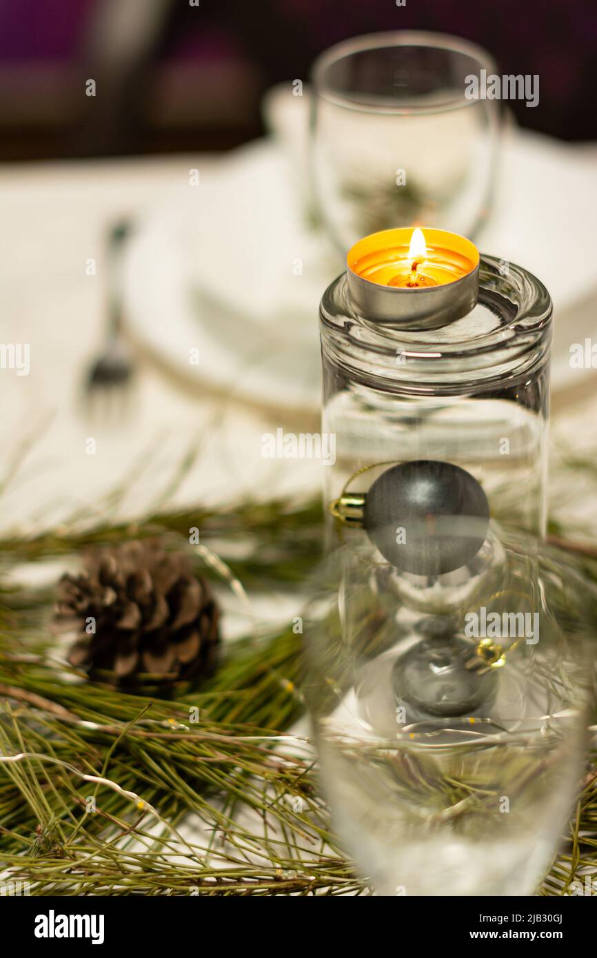 Elementi decorativi su un tavolo di Natale con luce soffusa da una candela del tè. Verticale Foto Stock