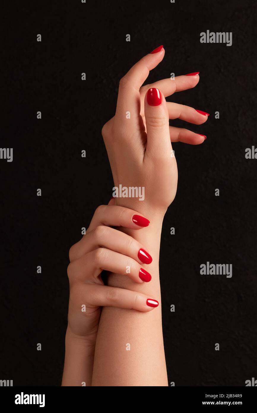 Mani femminili con manicure bello - chiodi rossi su sfondo nero scuro. Unghie, concetto di cura della pelle Foto Stock