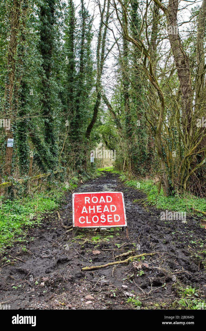 Strada davanti al segnale di avvertimento di traffico chiuso su strada fangosa nella campagna di Cheshire Foto Stock