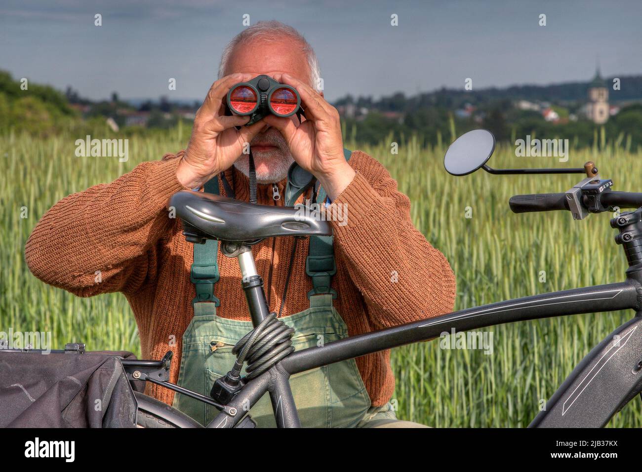 Hunter si inginocchia dietro la bicicletta e guarda la zona di caccia attraverso il suo binocolo. Foto Stock