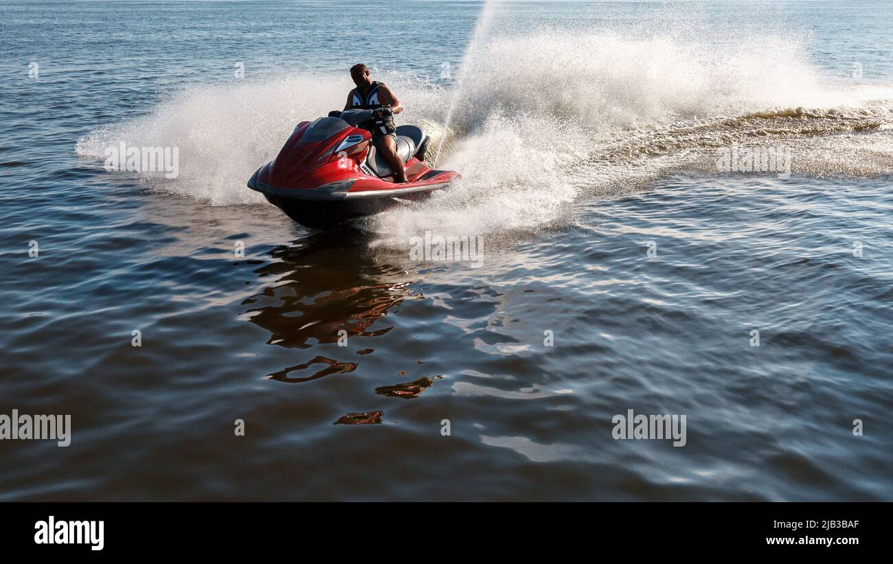 L'uomo guida il jet ski rosso sul mare turchese in un giorno blu Foto Stock