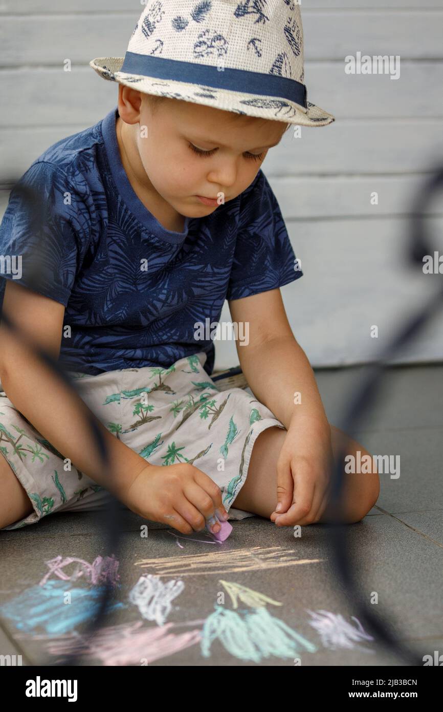 Piccolo ragazzo preschool disegna con gessetti colorati a terra. Il bambino è molto concentrato sull'apprendimento. Foto Stock