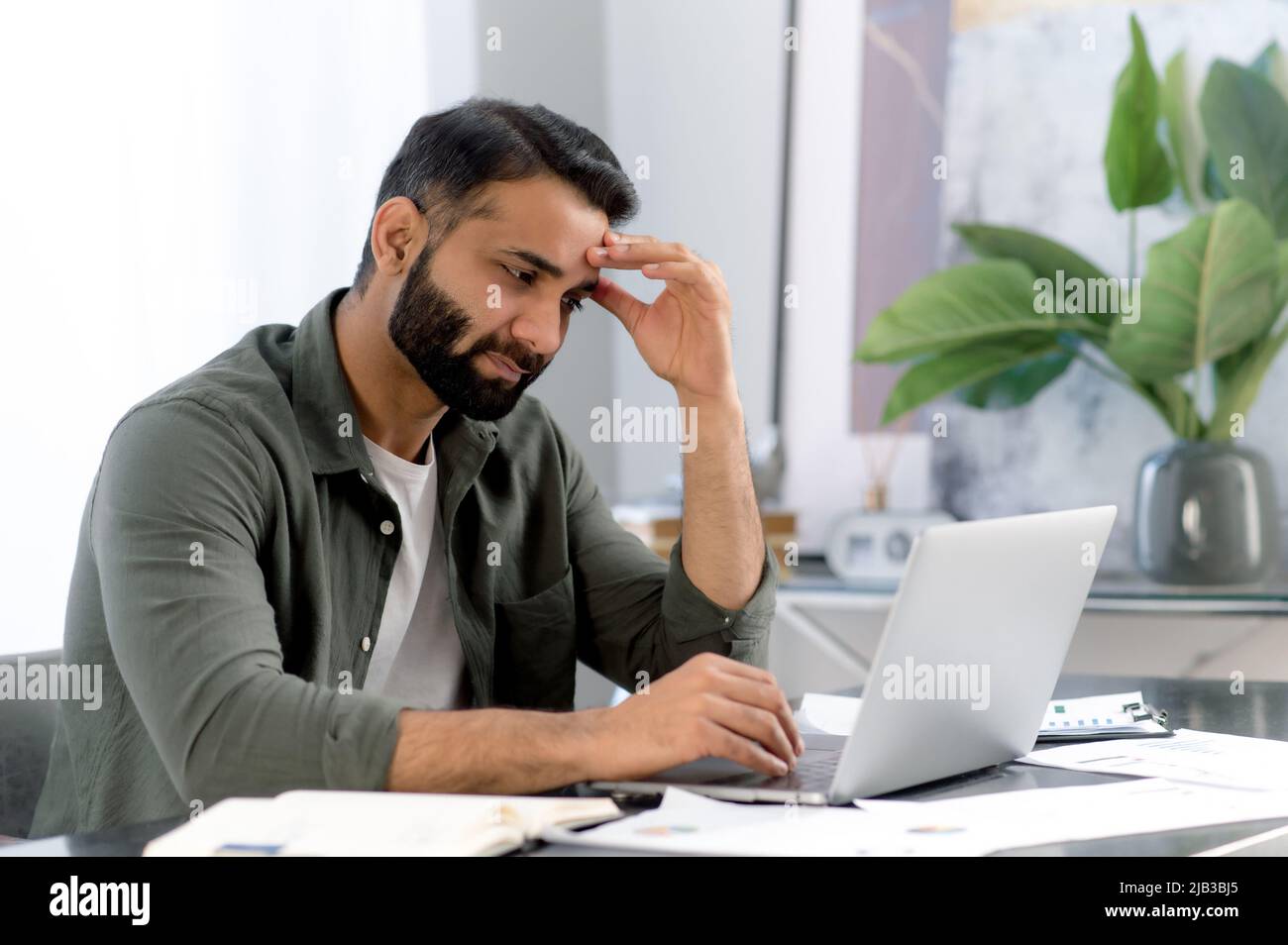 L'uomo arrabbiato arabo o indiano, stanco, sovraccaricato di lavoro in un computer portatile, guarda tristemente allo schermo, è sottolineato a causa di un lavoro non fatto in tempo, un progetto fallito, una startup, ha bisogno di una vacanza Foto Stock