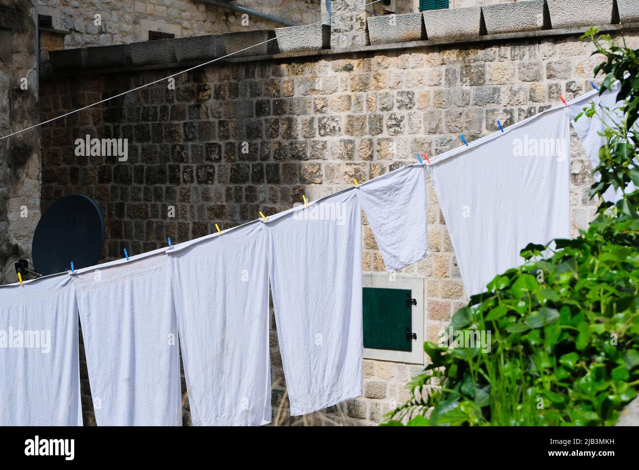 bianco pulito bucato che asciuga su una linea di clothesline all'aperto al sole al vecchio sfondo della parete di pietra, modello di pulizia creativa con spazio di copia Foto Stock