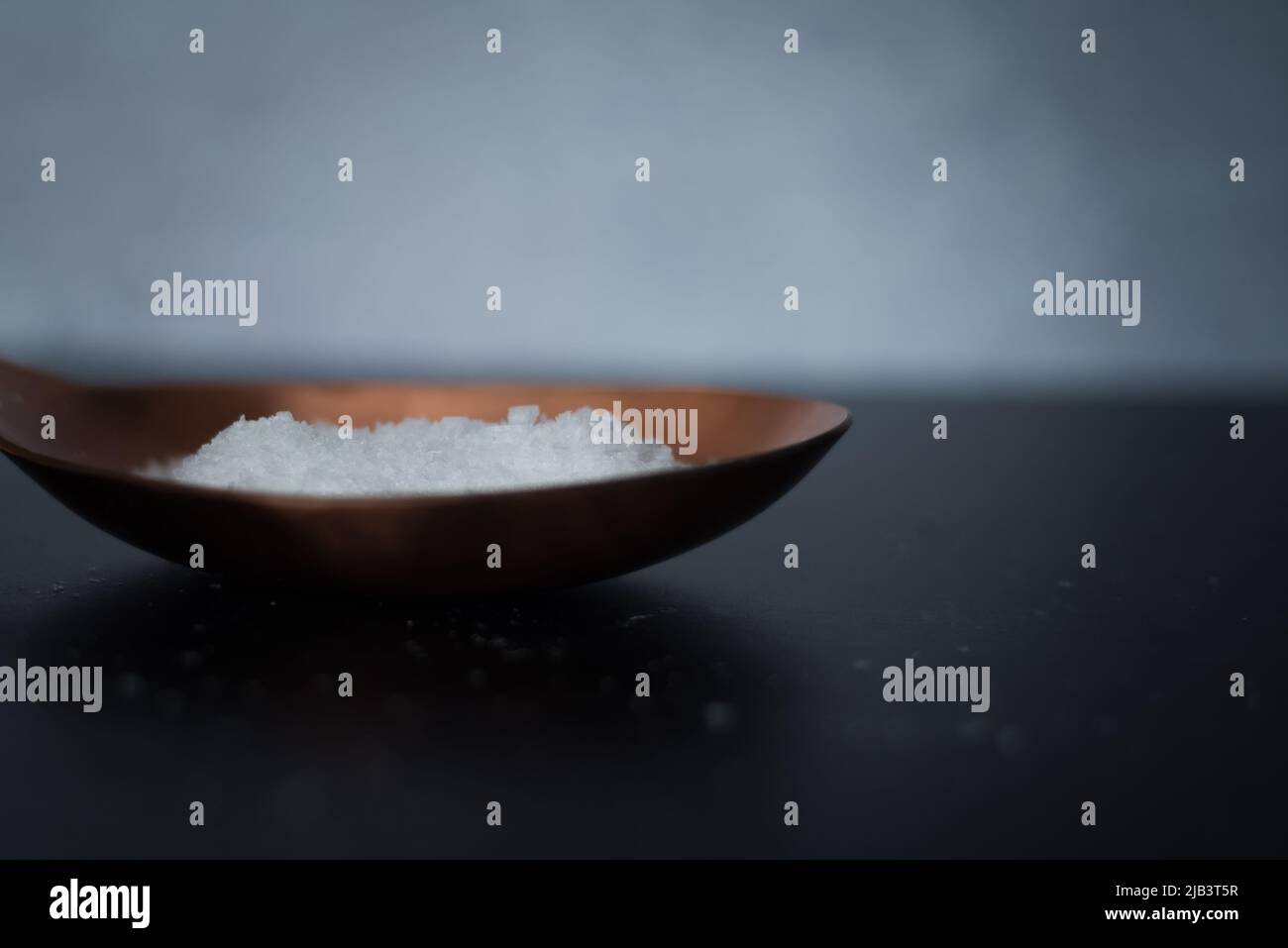 Vista laterale del sale marino organico in cucchiaio di rame su sfondo scuro. Foto Stock
