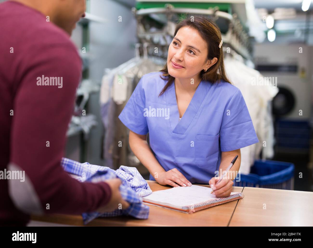 Donna addetto alla pulitura a secco che riceve i vestiti dal cliente Foto Stock